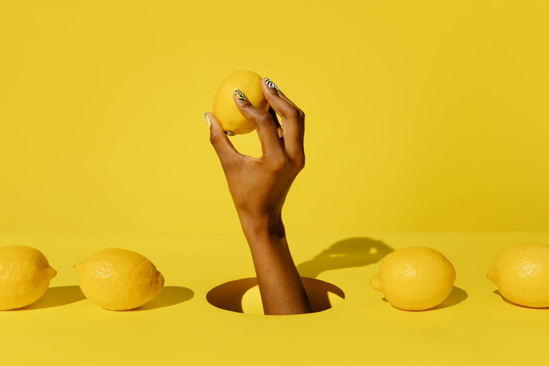 Hand holding a bright lemon against yellow background, representing fresh pleasure and the lemon vibrator experience