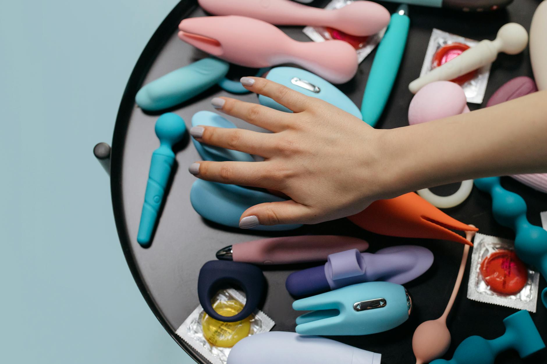A hand reaching over a variety of colorful lemon vibrators and clitoral toys arranged on a table.