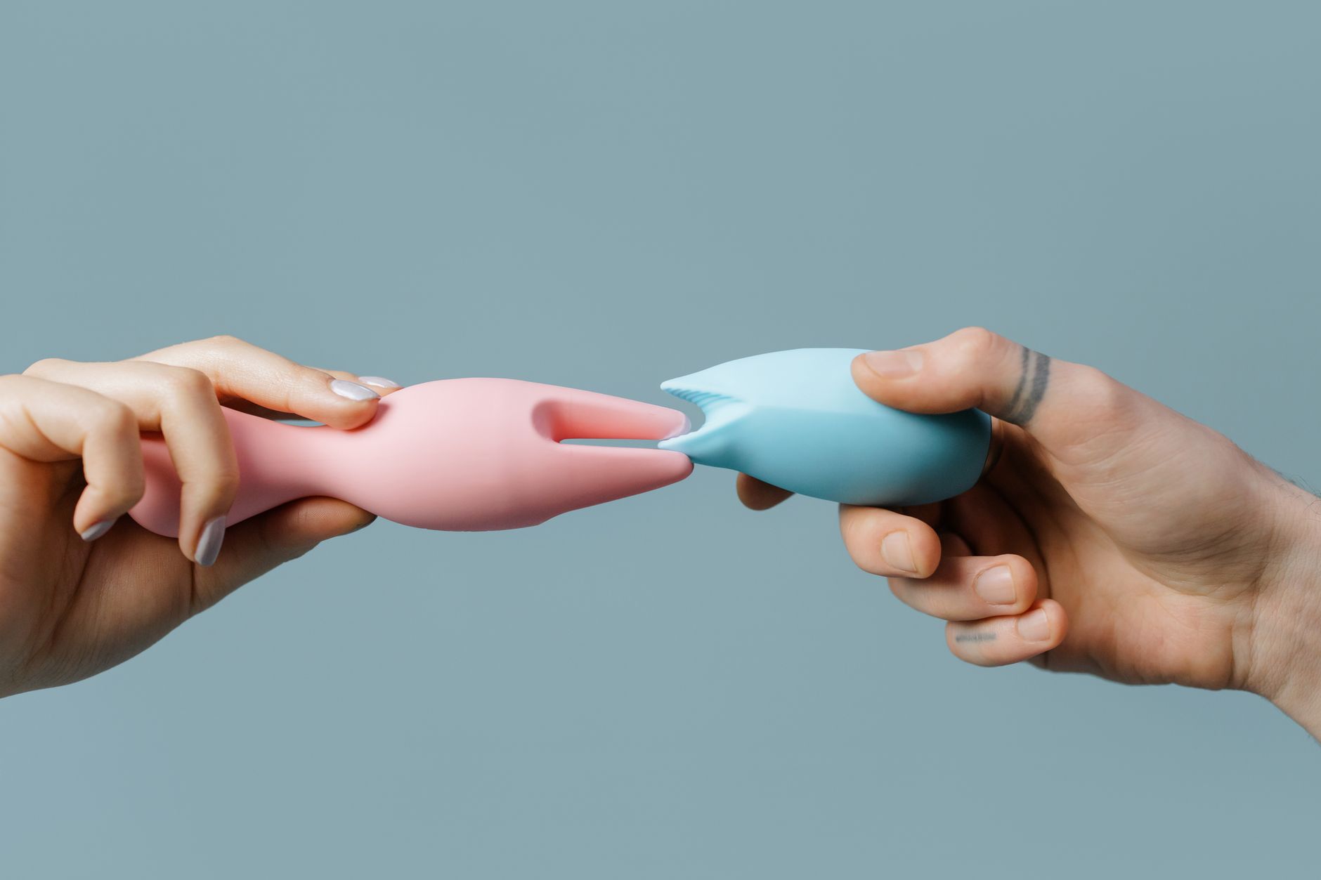 Close-up of hands holding silicone pleasure toys in soft pastels, representing partnership and shared intimacy