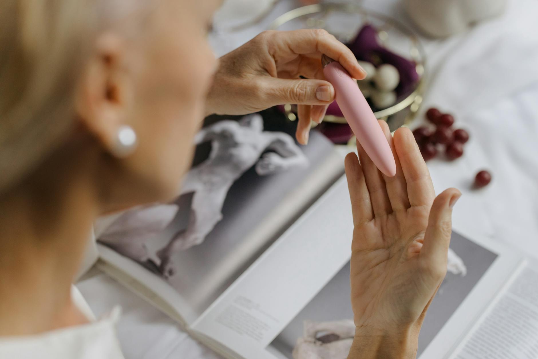 Close-up of hands exploring an intimate moment with a clitoral toy, surrounded by personal items suggesting comfort and self-care.
