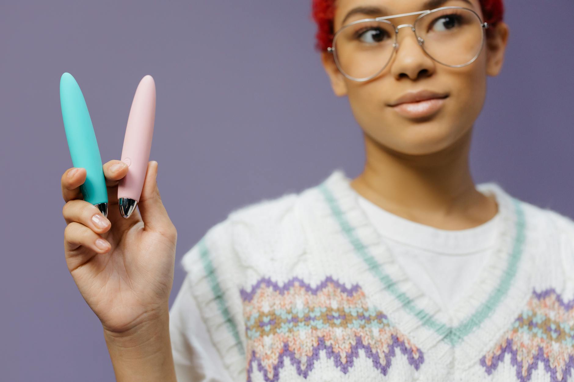 Two colorful vibrators held against a purple background, representing modern pleasure tools.