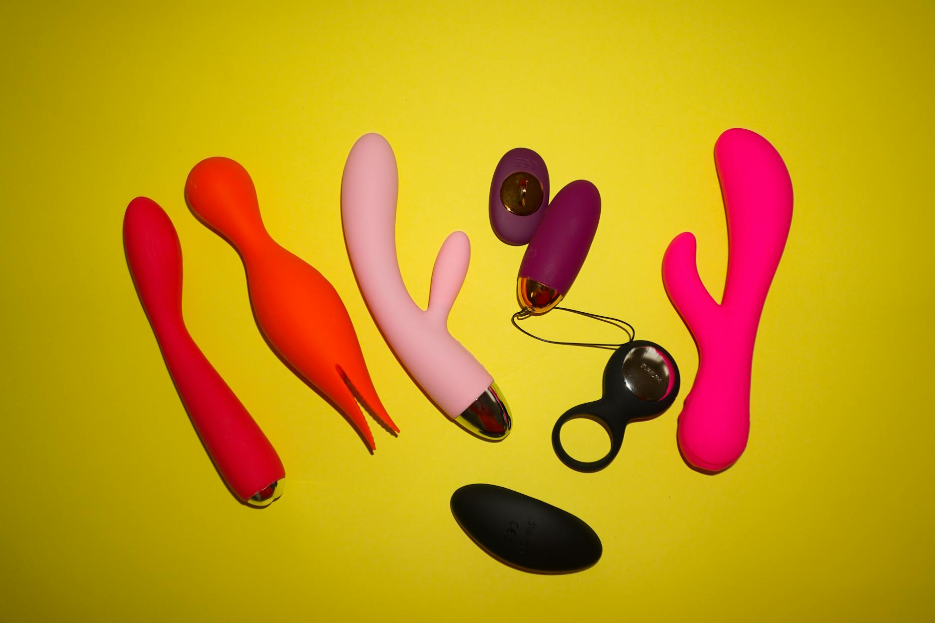 Two hands holding pink and blue silicone vibrators together against a pastel background